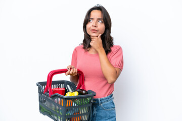 Fototapeta na wymiar Young woman holding a shopping basket full of food having doubts
