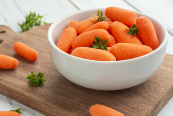 Baby carrots in a bowl over wooden table with herbs