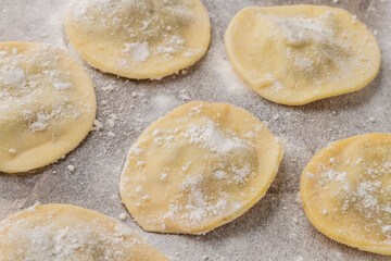 Uncooked stuffed raviolonis or raviolis with flour with ingredients over wooden table