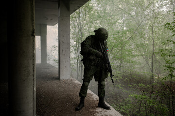 Military soldier in uniform standing with a weapon in his hands in a dark room on the outskirts of the forest