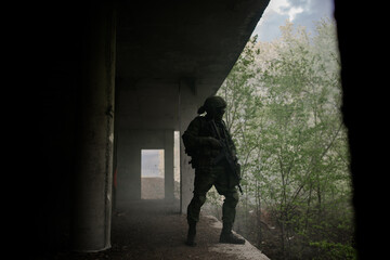 Military soldier in uniform standing with a weapon in his hands in a dark room guarding a military...