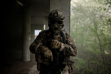 Obraz premium Military soldier in uniform standing with a weapon in his hands at night. Dark portrait of a military man
