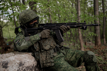 Russian military soldier in uniform sitting in the forest, firing a weapon