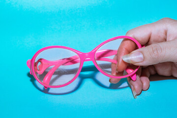 hand of young latin woman, with long fingernails, holding a pair of pink glasses, blue background....