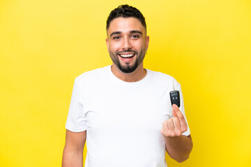 Young Arab man holding car keys isolated on yellow background with surprise and shocked facial...