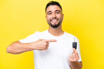 Young Arab man holding car keys isolated on yellow background and pointing it