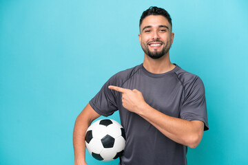 Young Arab handsome man isolated on blue background with soccer ball and pointing to the lateral
