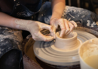 A woman works on a potter's wheel. Hands form a cup of wet clay on a potter's wheel. Artistic concept.