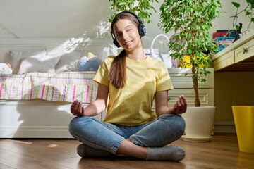 Teenage girl in headphones relaxing sitting in lotus position at home