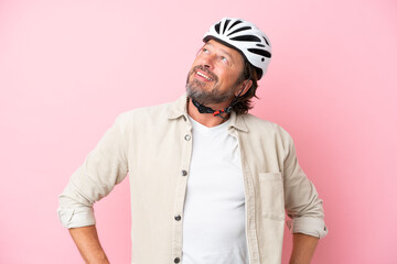 Senior dutch man with bike helmet isolated on pink background posing with arms at hip and smiling