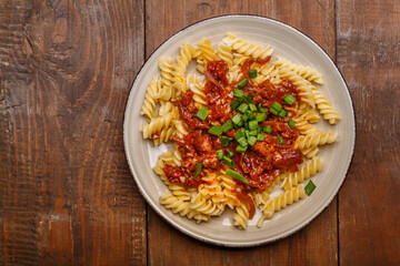 Plate with bolognese pasta on a wooden table sprinkled with green onions.