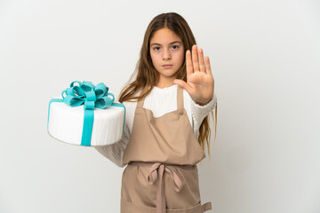 Little girl holding a big cake over isolated white background making stop gesture