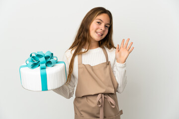 Little girl holding a big cake over isolated white background saluting with hand with happy expression