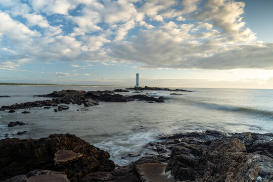 Sunrise with long exposure photograph of the beach with lighthouse on the horizon