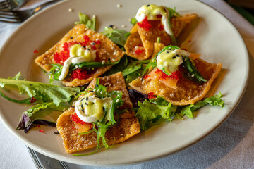 selective focus on smoked salmon nachos with salmon, caviar, and seaweed salad on a white plate