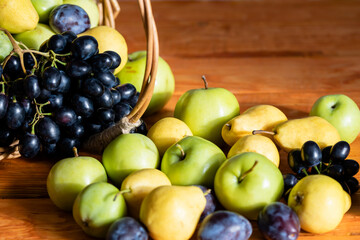 Basket with ripe fruits: apples, pears, grapes, plums selective focus