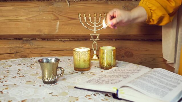 The hand of a Jewish woman lights candles in honor of Shabbat on the siddur table. Overall plan
