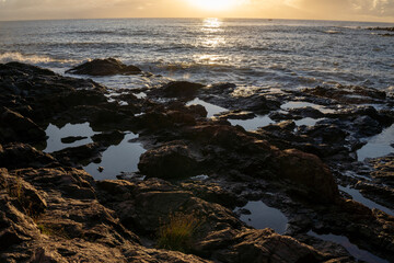 Sun rising on the sea horizon behind rocks on the beach