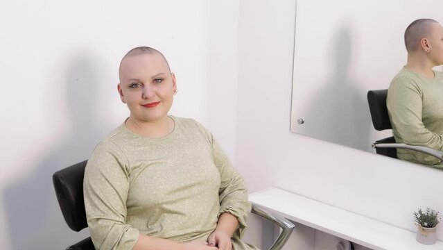 A woman in a barbershop shaved bald smiling looking at the camera. Medium plan