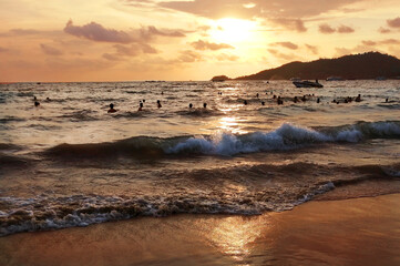Coast with waves in the sea at sunset. Unrecognizable people bathe in the waves during sunset.