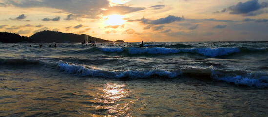 Fototapeta na wymiar Coast with waves in the sea at sunset. Unrecognizable people bathe in the waves during sunset.