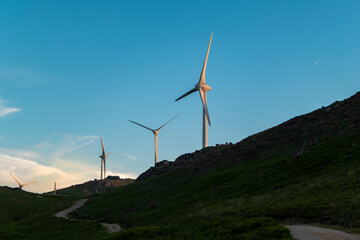 Turbinas eólicas na paisagem montanhosa ao pôr do sol com uma estrada sobre a montanha - obrazy, fototapety, plakaty
