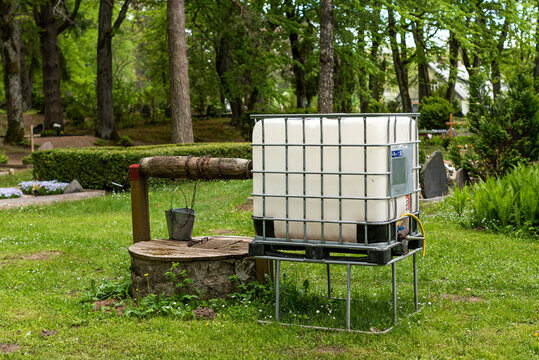 White plastic water tank cube with a metal frame and well in cemetery.