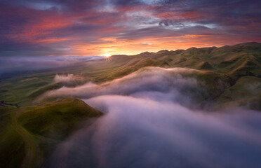 Dramatic sunrise above patchy fog in rolling hills, Central California, USA