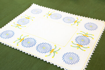 White linen napkin with machine embroidery in the form of cornflowers, with an openwork border, on a green linen background. A decorative detail for the interior in an authentic style.