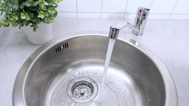 A stream of clean water drink flows from the kitchen faucet into the stainless steel sink. Environment, water pollution and water shortage concept