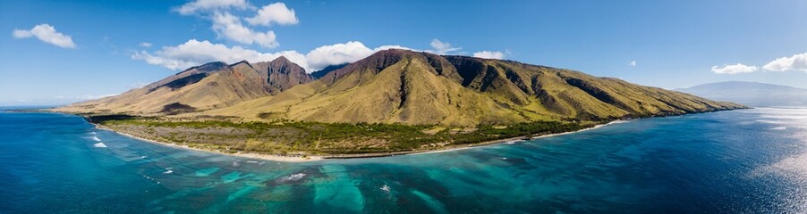 Aerial panorama drone view of the West Maui Mountains along west coast of Maui with clear blue ocean water and coral reef and green mountain on the background. Maui, Hawaii