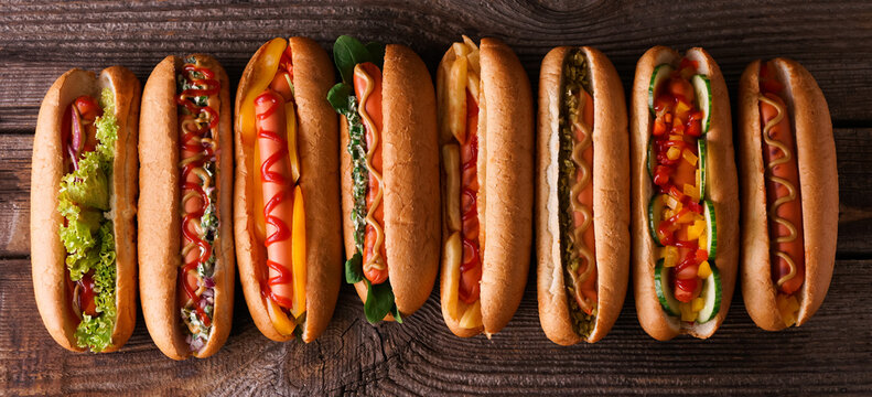 Many tasty hot dogs on wooden background, top view
