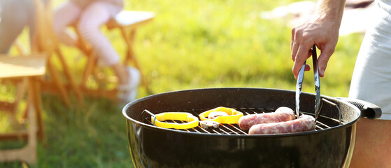 Man cooking sausages and vegetables on barbecue grill outdoors, closeup