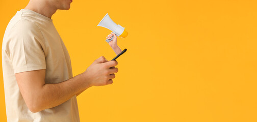 Young man with mobile phone and hand holding megaphone against yellow background