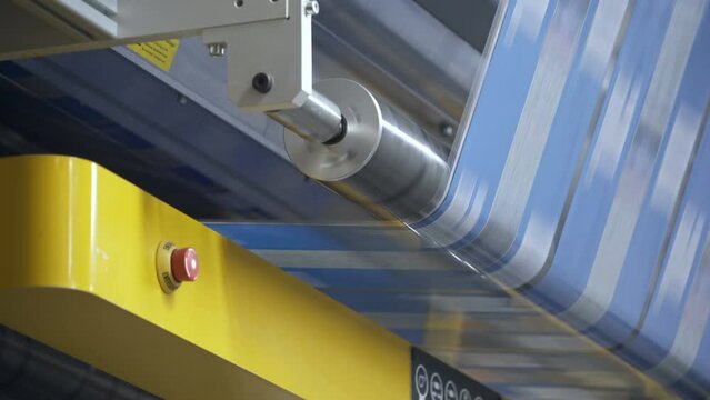 Printing house. Flexo printing. Roller machine prints. Film spins around shaft. Roller rotates rapidly.