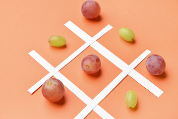 Game of Tic-tac-toe with fresh grapes on color background