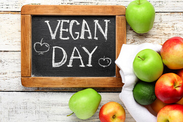 Bowl with fruits and board with text VEGAN DAY on white wooden background