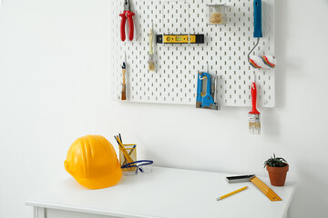 Pegboard with modern tools and desk near light wall