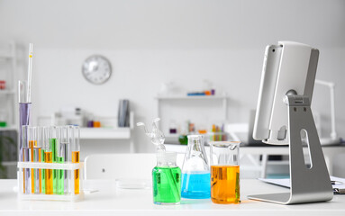 Microscope, tablet computer and chemical glassware on table in medical laboratory
