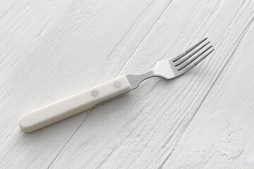 Stylish stainless steel fork on white wooden background