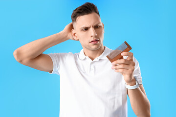 Young man with hair loss problem and comb on blue background