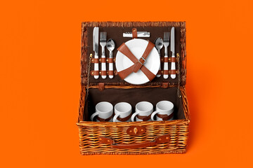 Wicker basket with tableware for picnic on red background