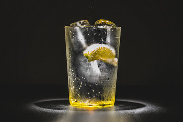 Large glass of gin and tonic, sparkling water, tonic soda with ice and a slice of lemon with a dark...
