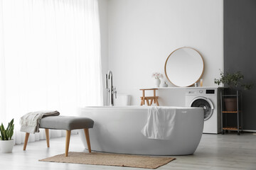 Fototapeta na wymiar Interior of light room with soft bench, bathtub and washing machine