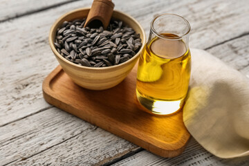 Bottle of oil, board, napkin and bowl with sunflower seeds on white wooden background