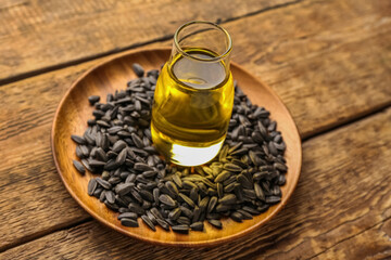 Plate with bottle of oil and sunflower seeds on wooden background