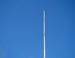 Empty white flagpole against the blue sky. Lowered flag. - obrazy, fototapety, plakaty