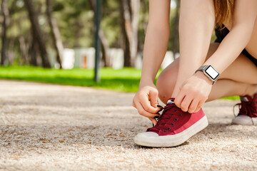 Naklejka premium Brunette sportive woman wearing black sports bra standing on city park, outdoors tying lace running shoes getting ready for run. Jogging girl exercise motivation health and fitness.