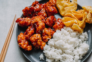 General Tsos Chicken with white rice and crab rangoon on a dark dish