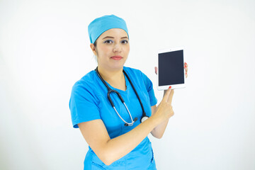 beautiful woman doctor, wearing blue uniform and blue surgical cap, stethoscope on her neck, using the tablet to display results on white background